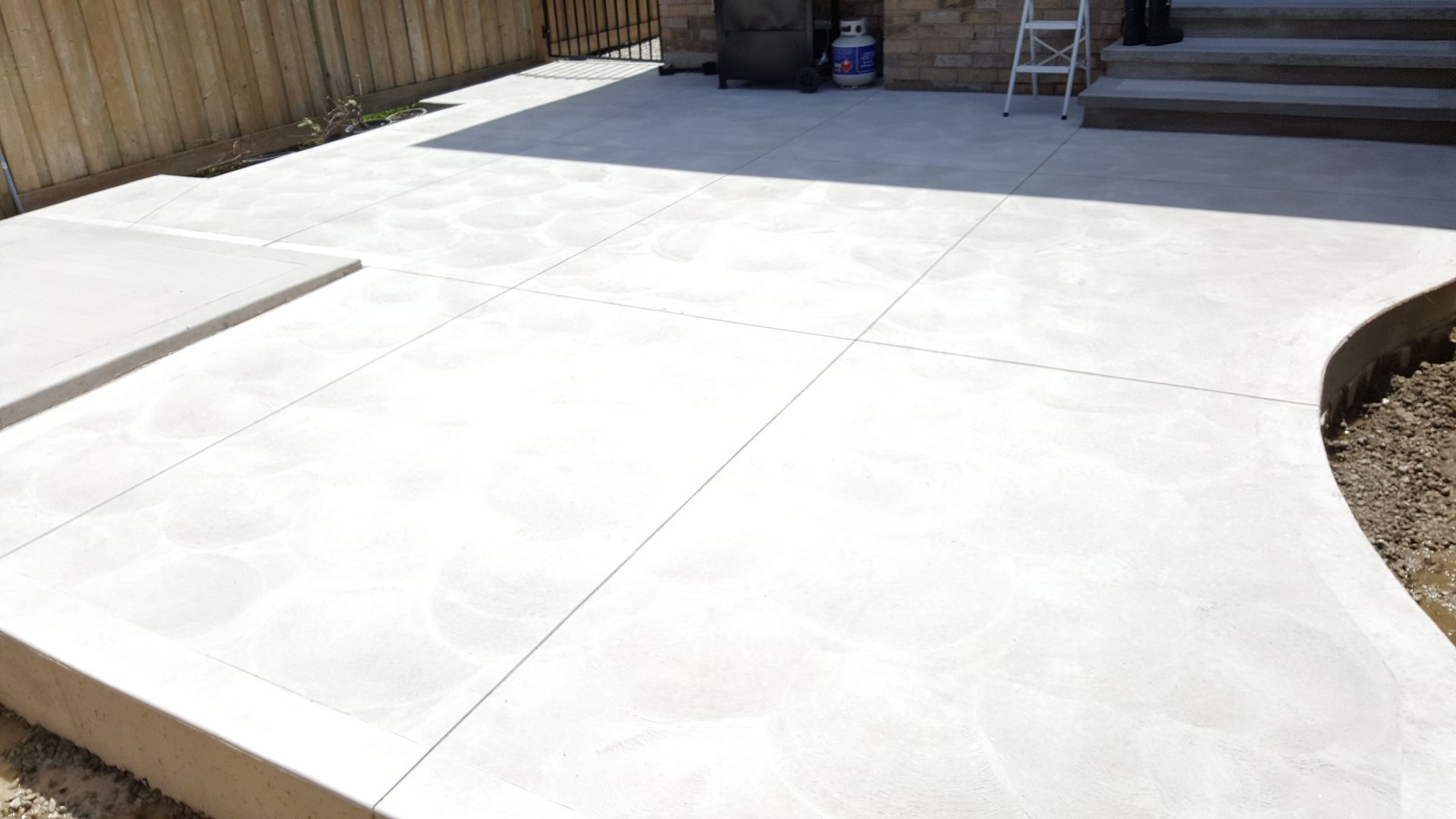 A white concrete patio with a wooden fence in the background.