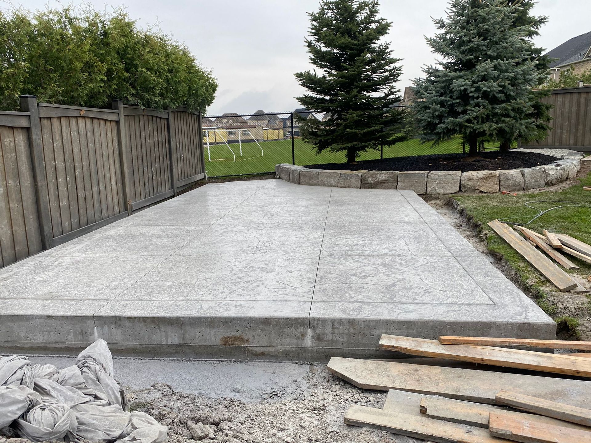 A concrete driveway is being built in a backyard next to a wooden fence.