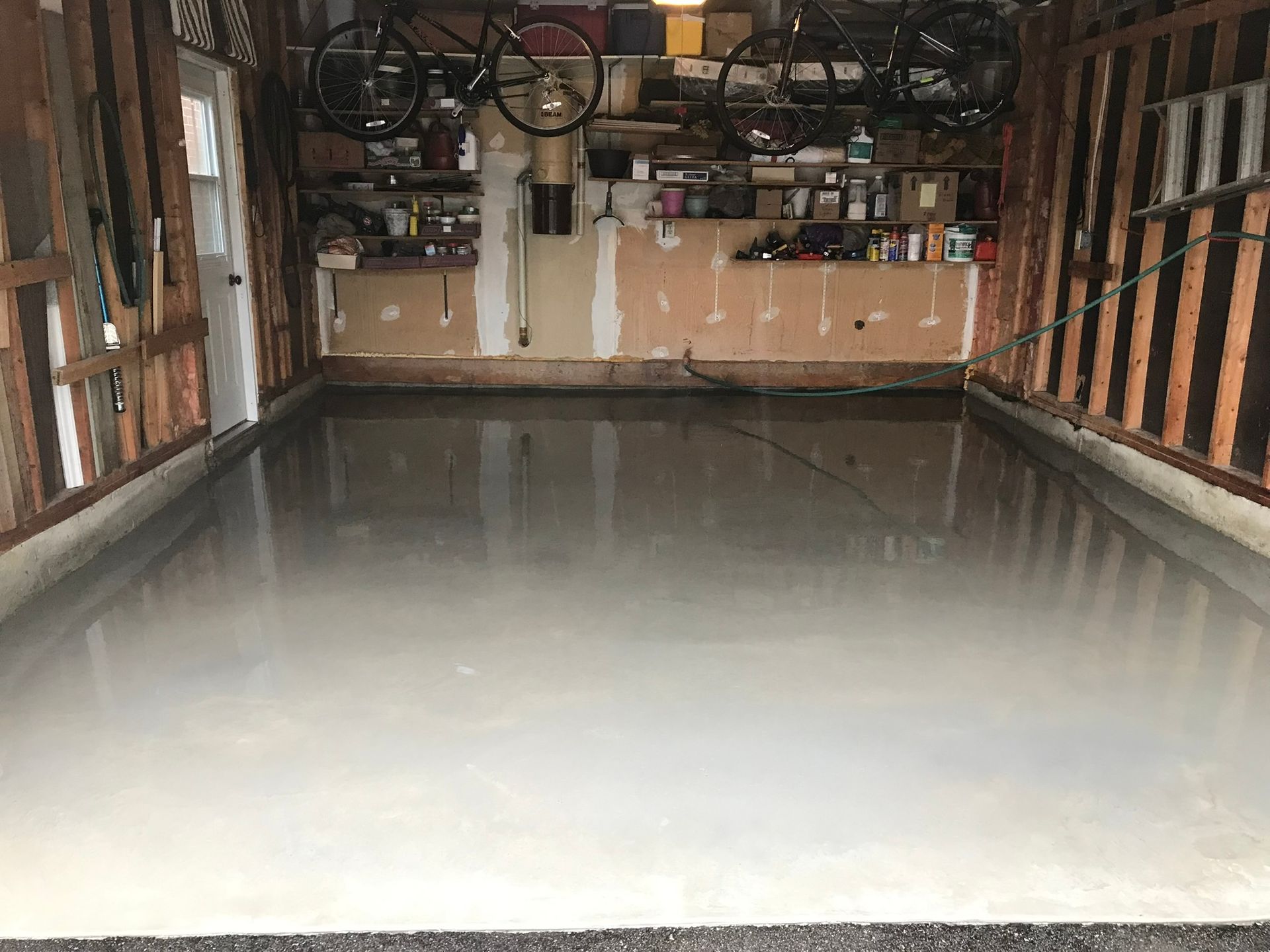 A garage with a concrete floor and a bicycle hanging from the ceiling.