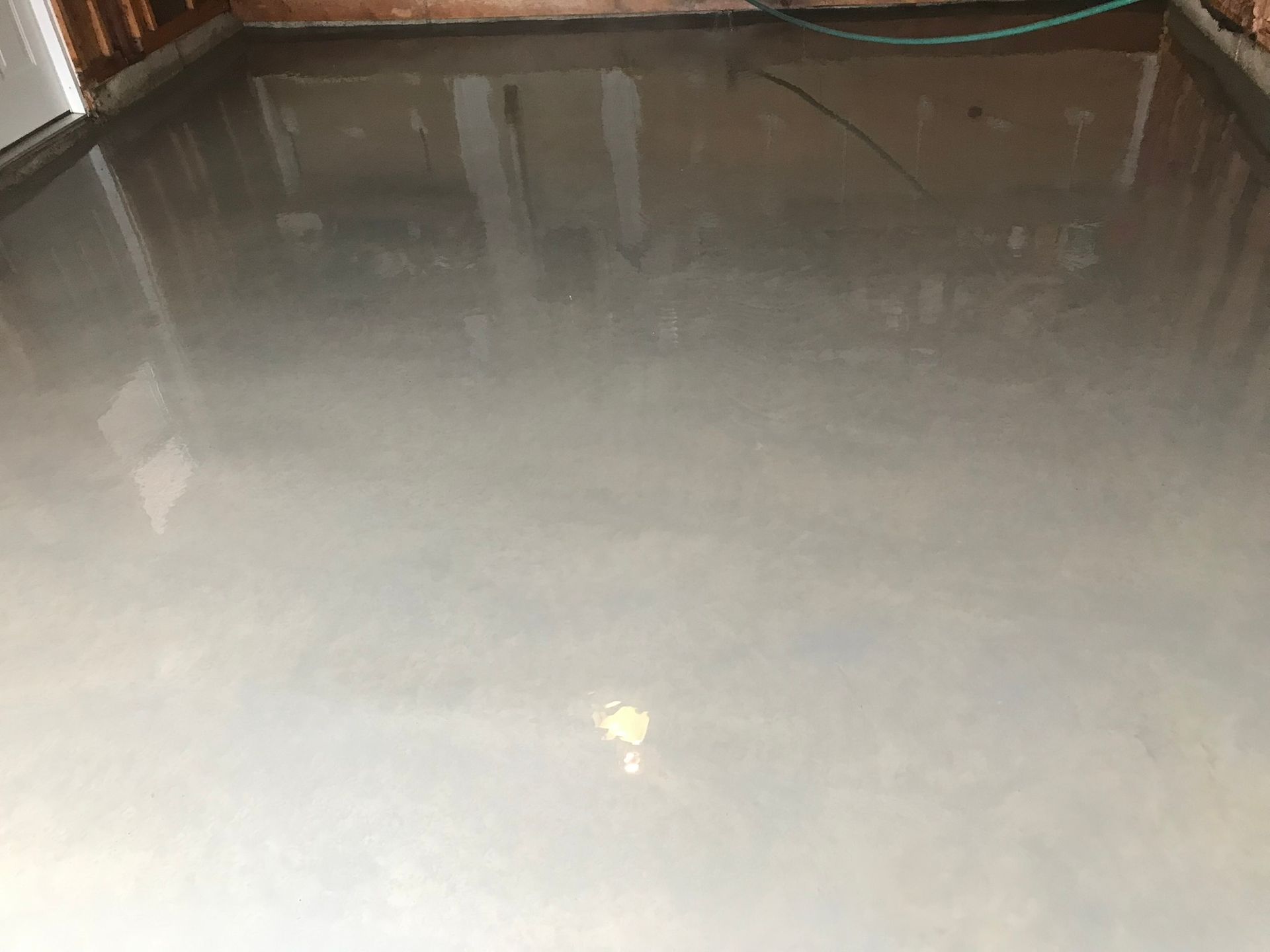 A shiny concrete floor in a garage with a green hose.