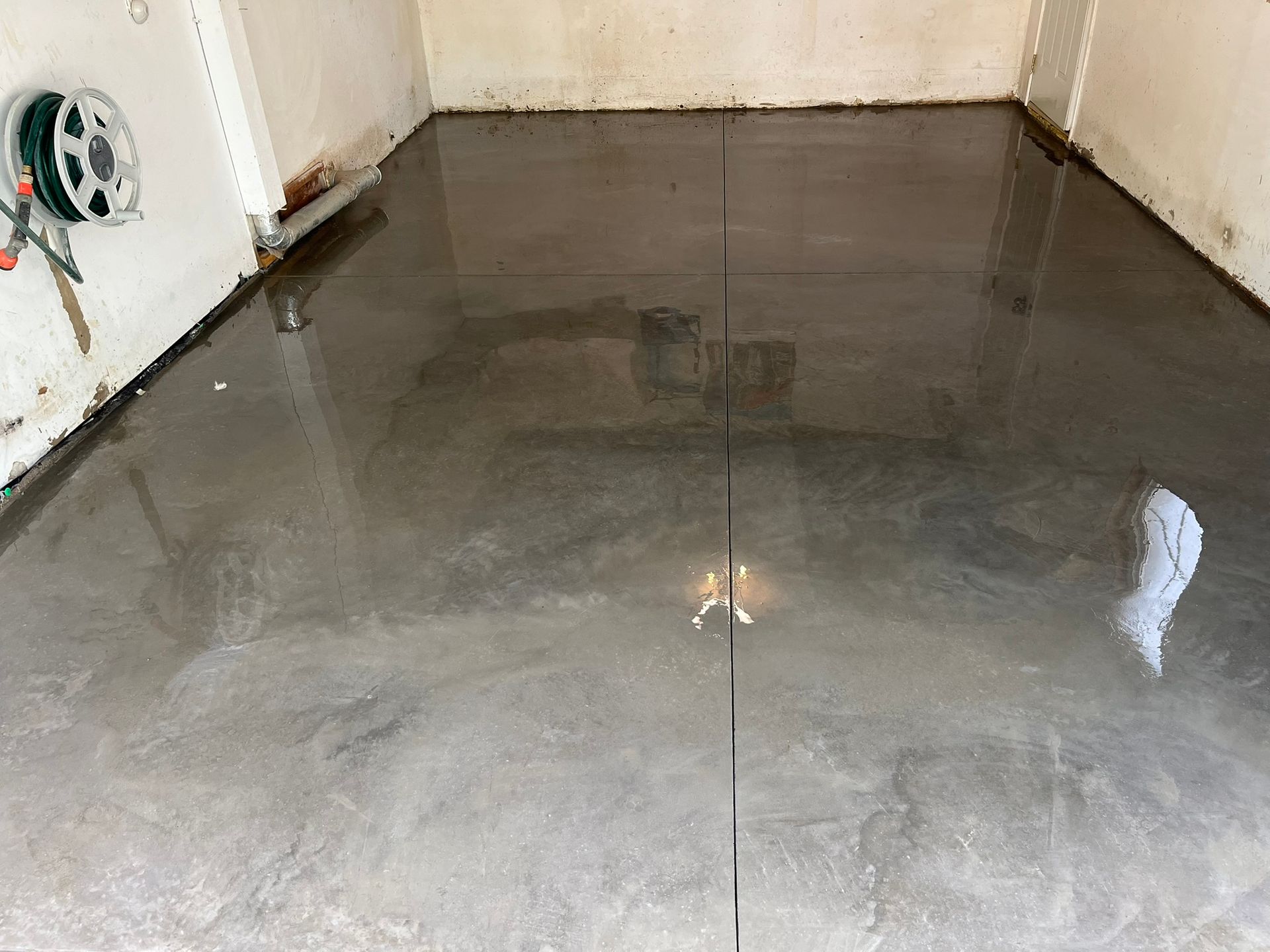 A concrete floor in a garage with a hose hanging on the wall.