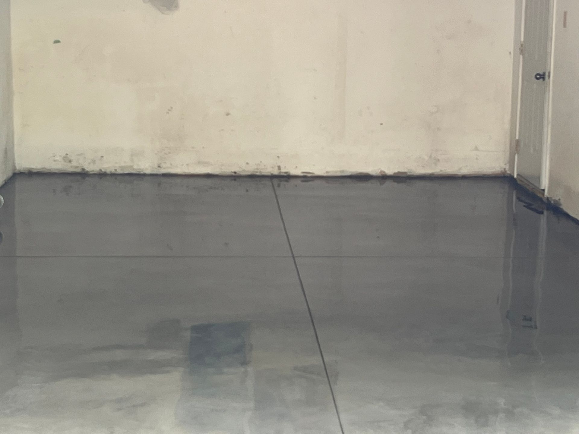 A concrete floor in a garage with a white wall and a door.