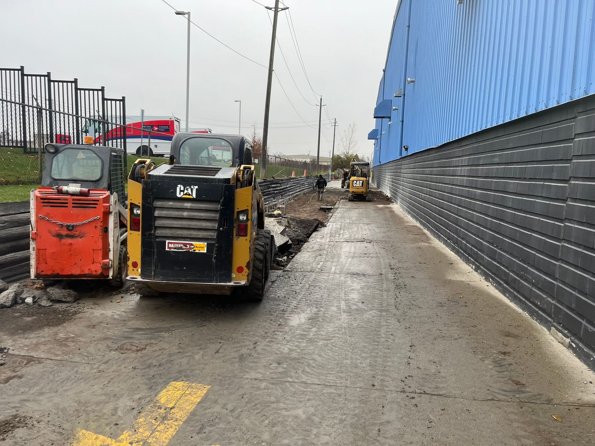 Two bulldozers are parked on the side of a road next to a building.