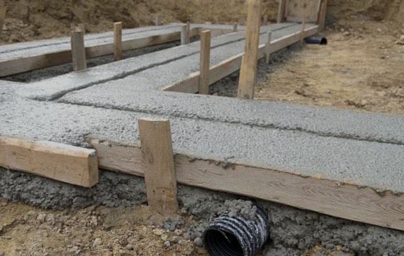 A pipe is laying on the ground next to a concrete foundation.