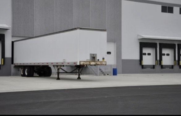A white semi truck is parked in front of a warehouse
