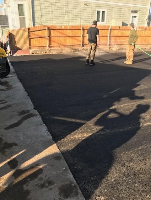 A couple of men are standing in a driveway with a hose.