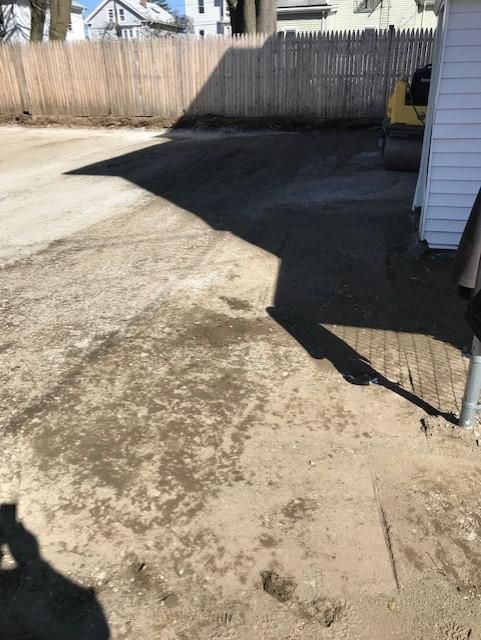 A dirt driveway in front of a house with a wooden fence.