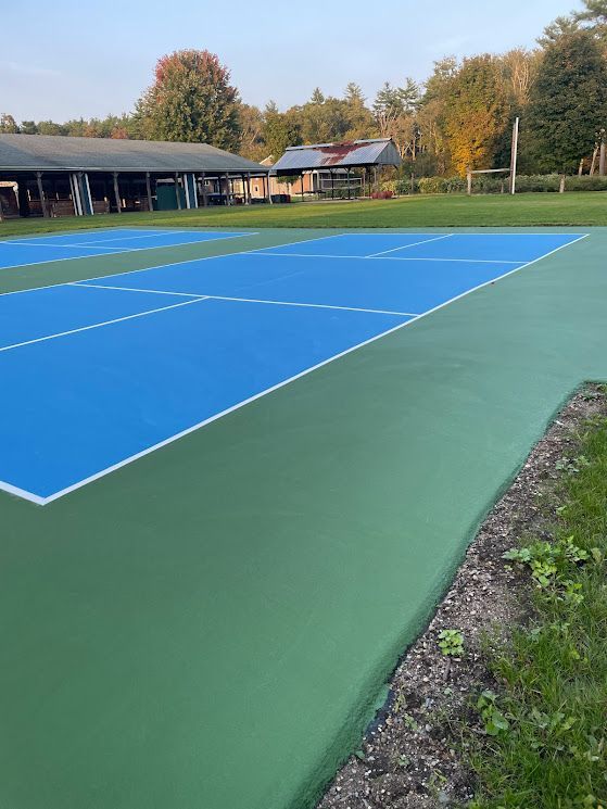 A blue and green tennis court with a building in the background.