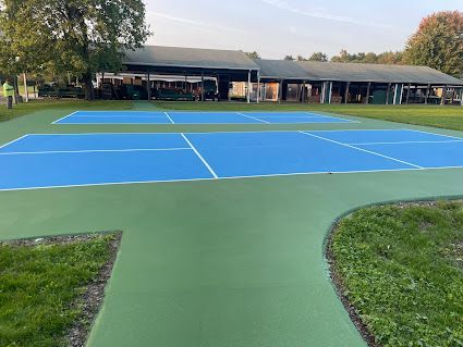 A couple of tennis courts in a park with a building in the background.