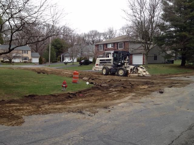 A bulldozer is working on a dirt road in front of a house.