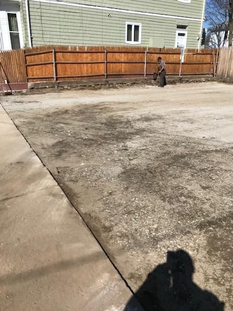 A concrete driveway with a wooden fence and a house in the background