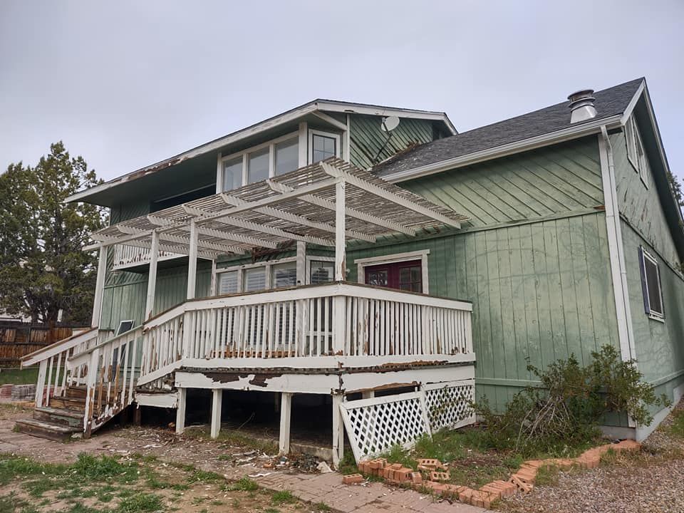 A green house with old paint and  a white deck and stairs.