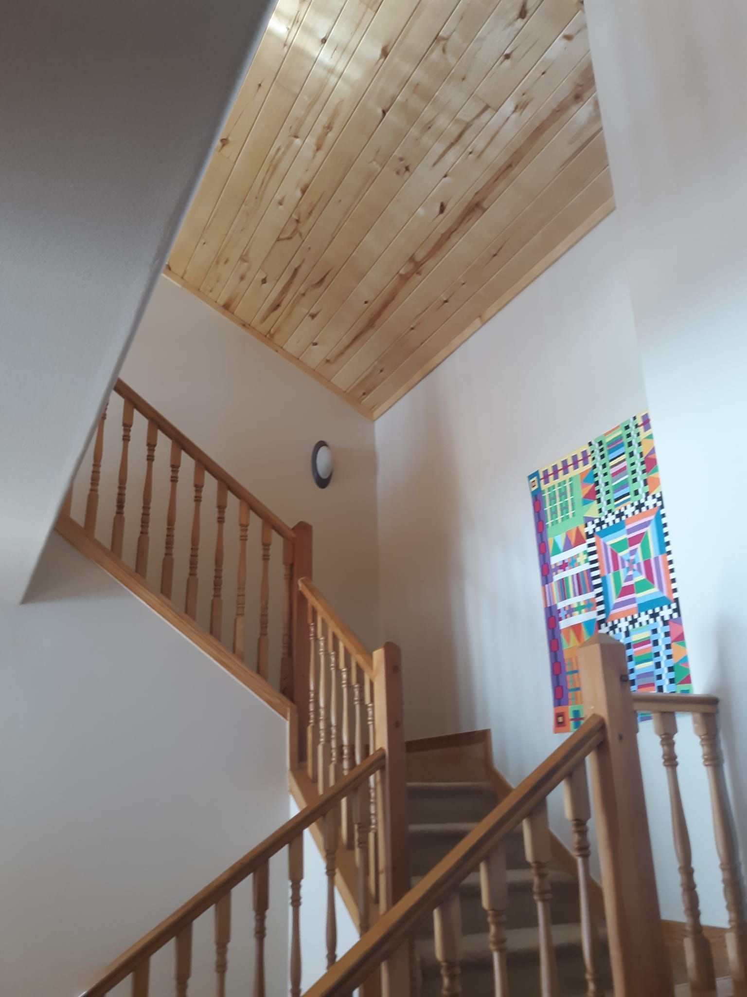 A staircase with new paint, and a wooden railing and a wooden ceiling