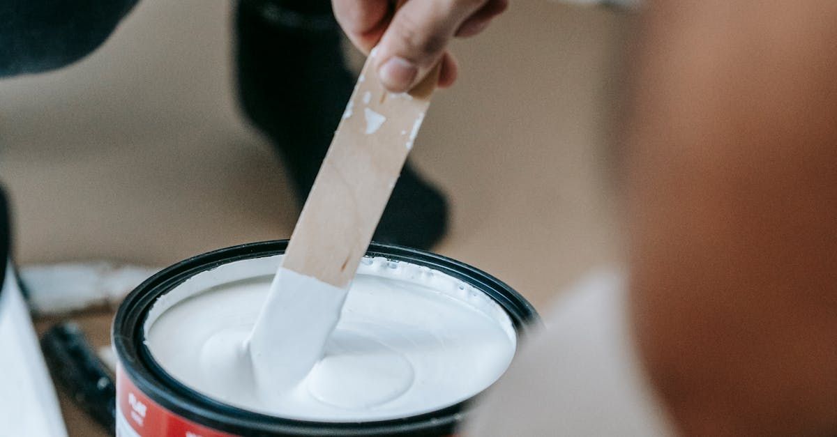 A person is mixing white paint in a can with a wooden spoon.