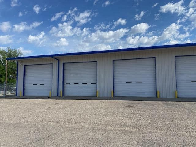A row of white garage doors on a freshly painted building with a blue roof.