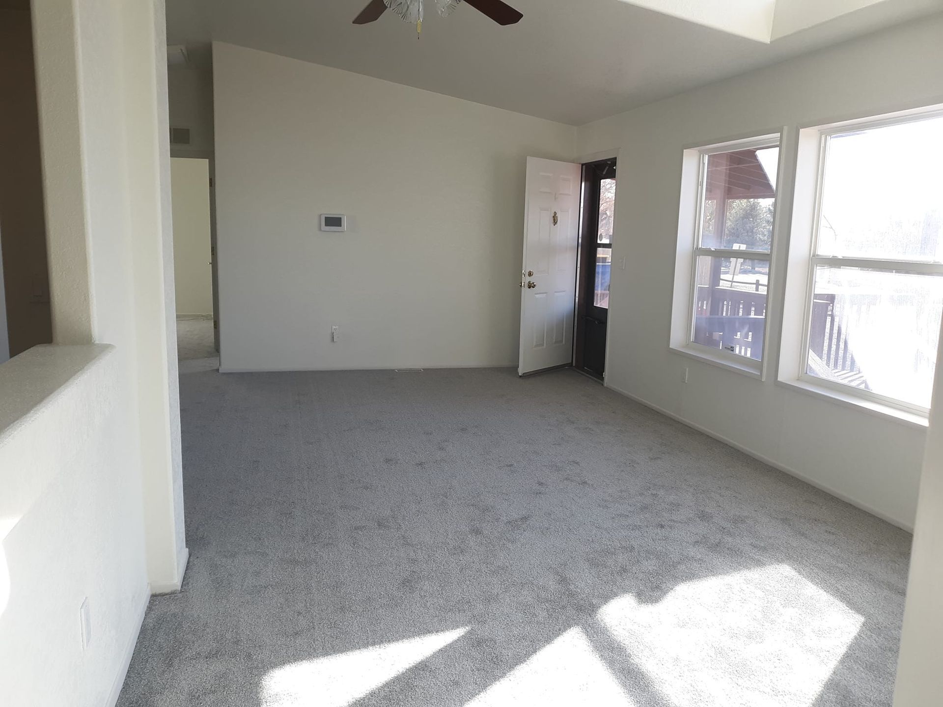 An empty living room with a ceiling fan and a lot of windows.