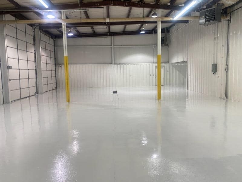 A large empty warehouse with a white floor and yellow poles.