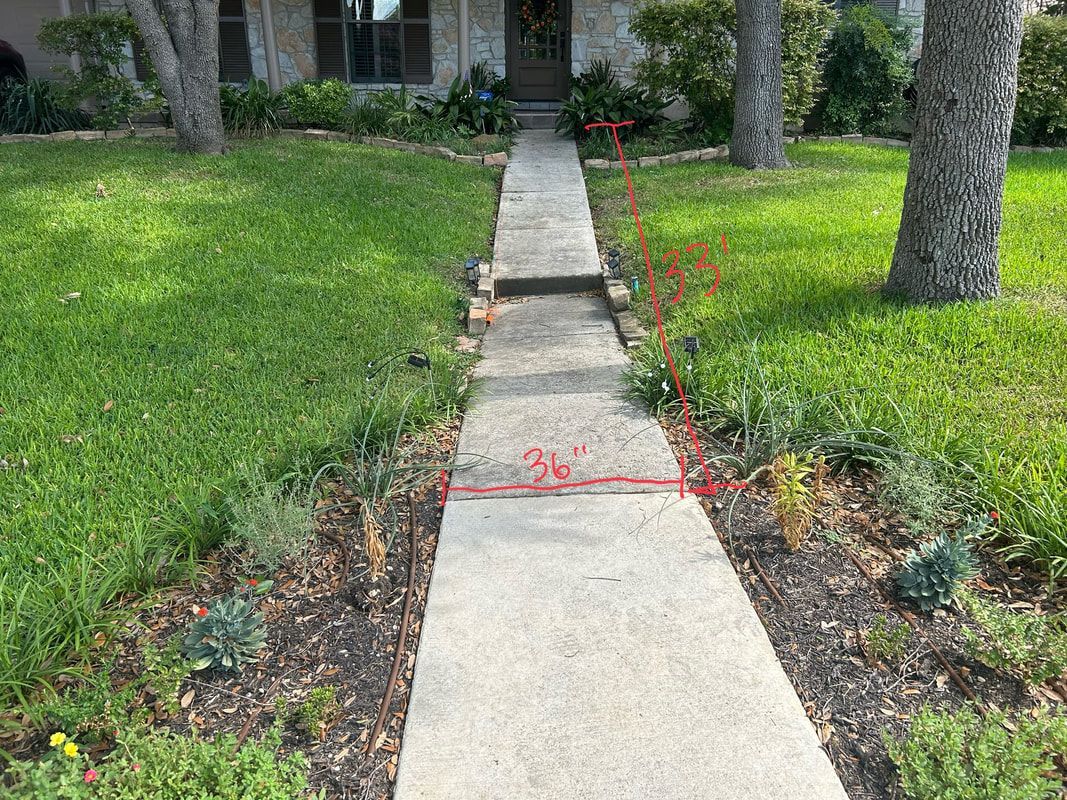 A concrete walkway leading to a house in a lush green yard.