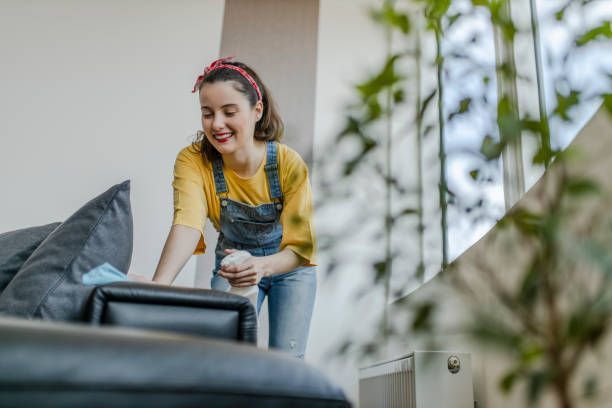 A woman is cleaning a couch in a living room.