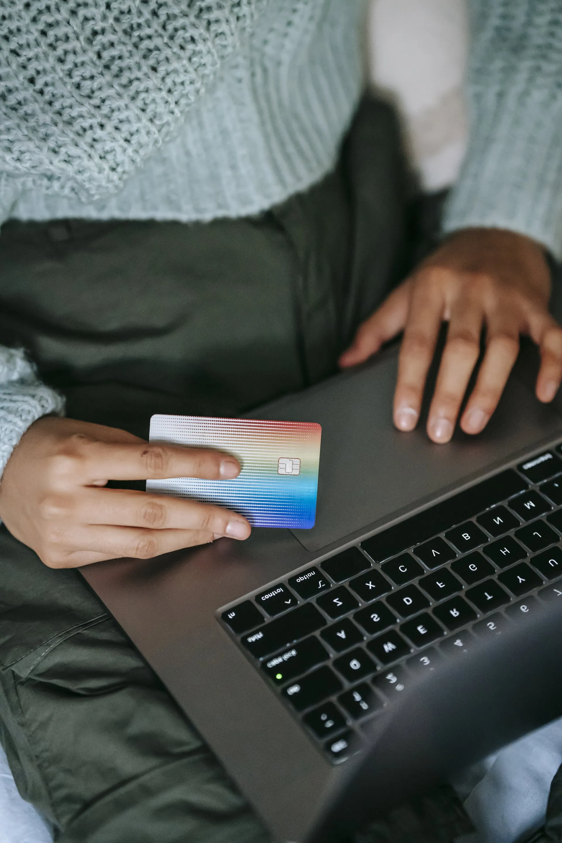 a person is holding a credit card while using a laptop computer .