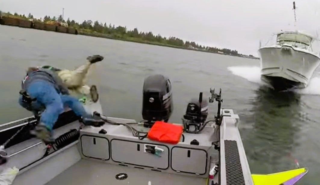 Man falls off a boat as a larger boat passes. Grey, overcast day.