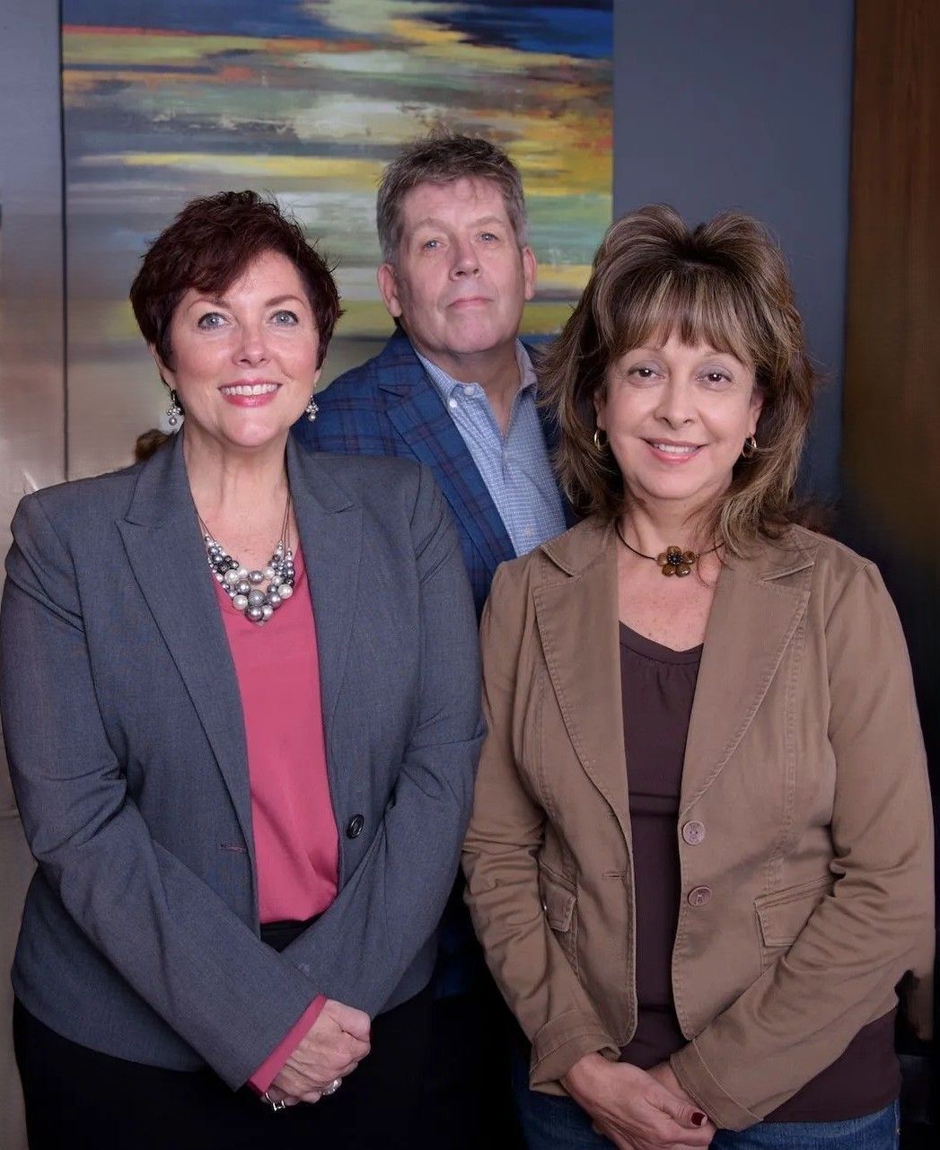 Three people in business attire standing indoors, smiling.