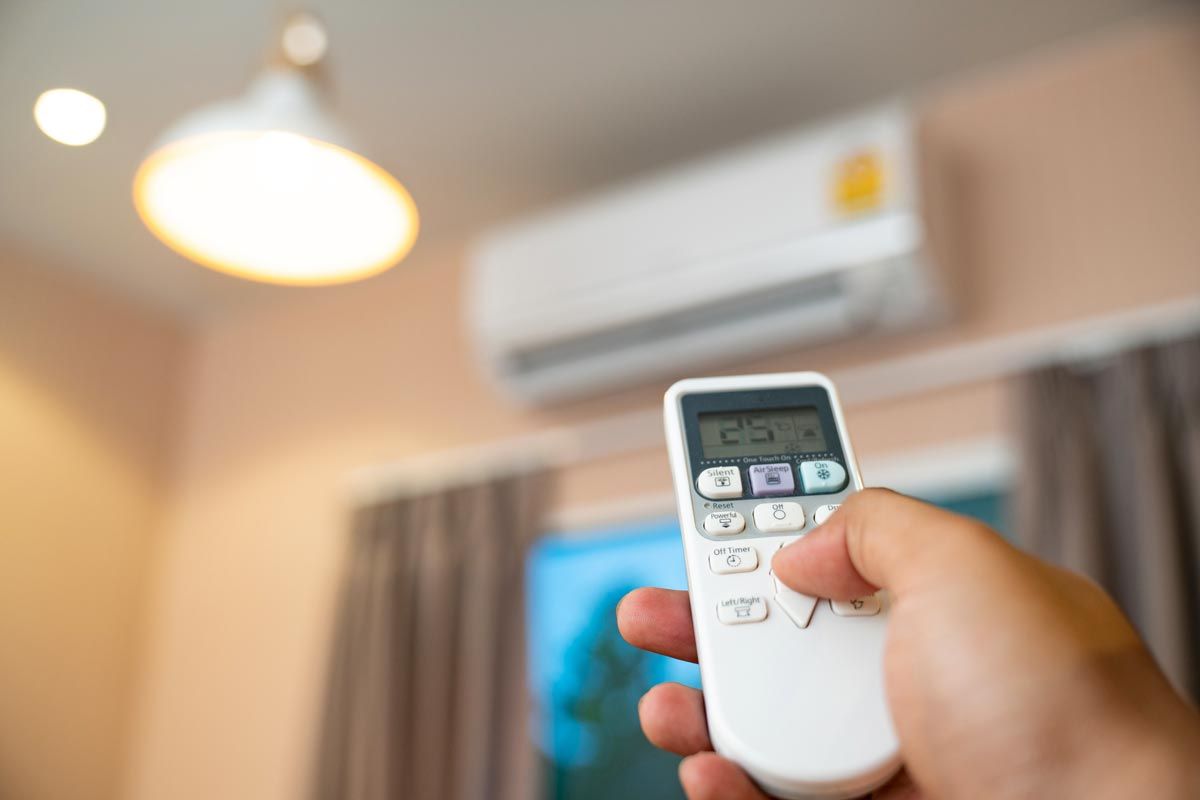 A person is holding a remote control in front of an air conditioner.