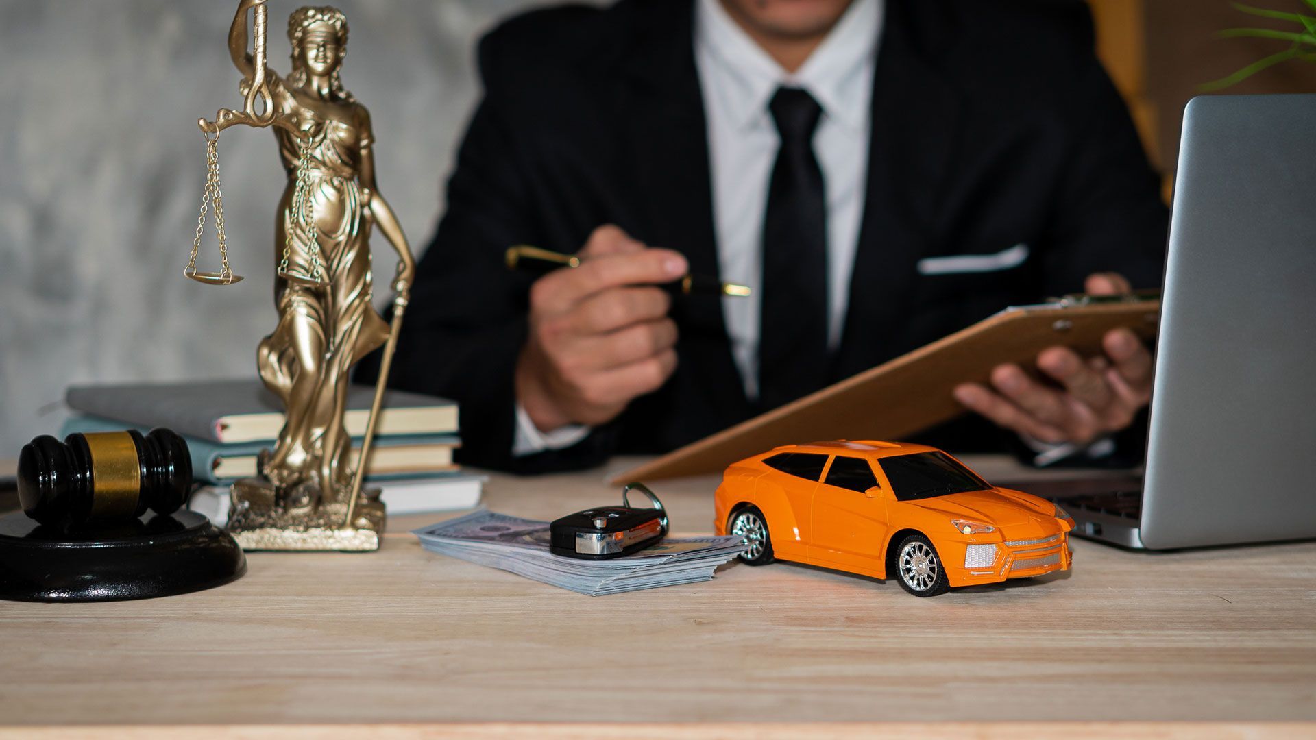 A lawyer with a justice statue, gavel, car model, and documents on a desk.