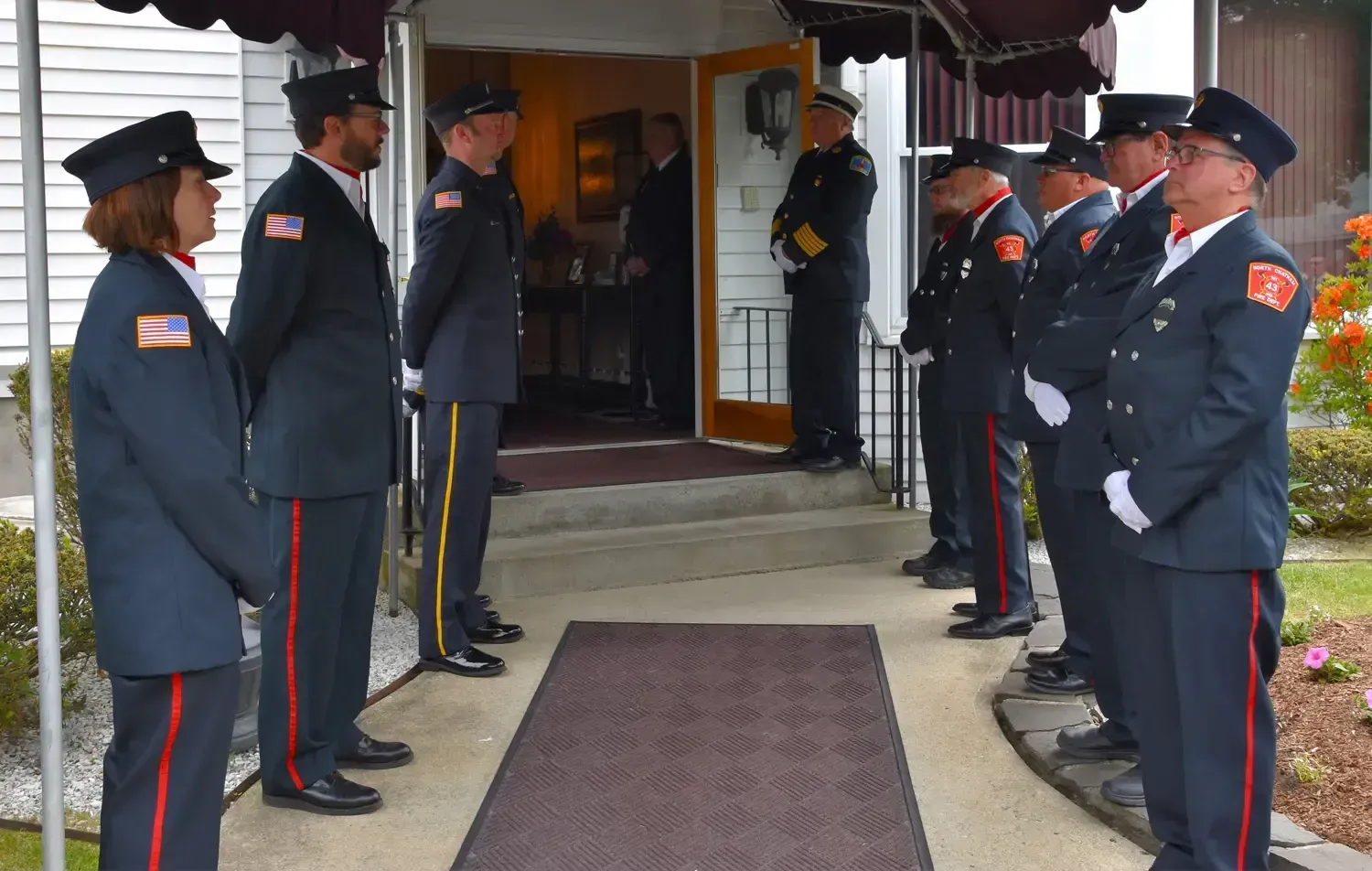 Firefighters in uniform standing outside a building, possibly for a ceremony.