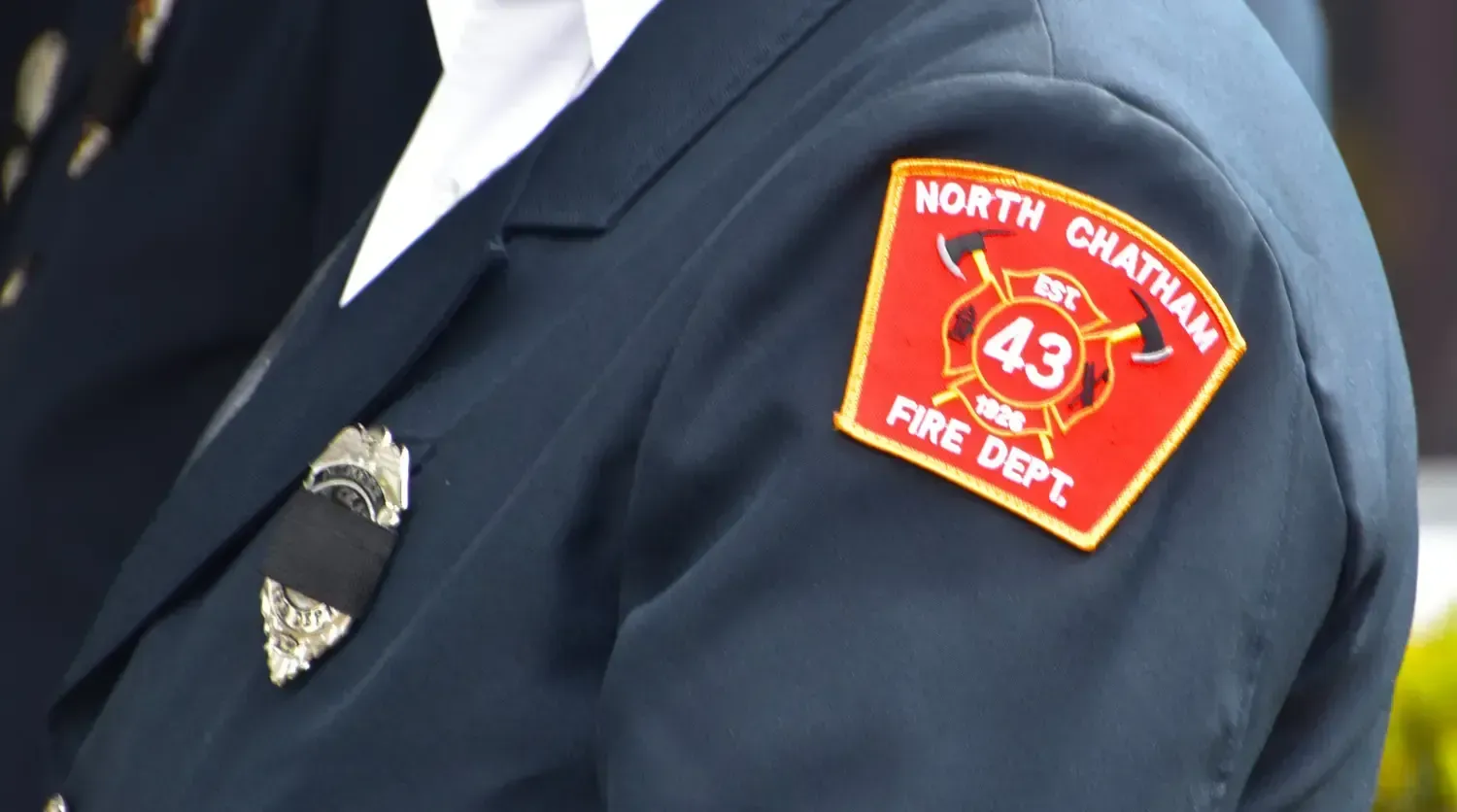 Shoulder of a navy blue uniform with a North Chatham Fire Dept. patch and badge.