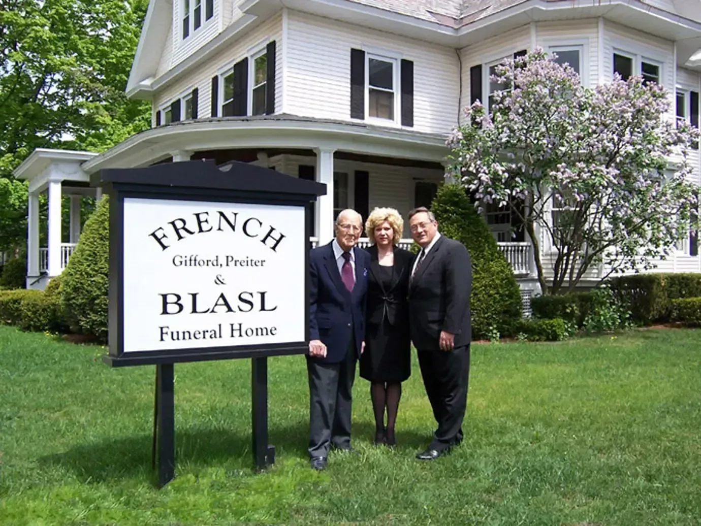 Sign for French & Blasl Funeral Home with three people standing in front of the building.