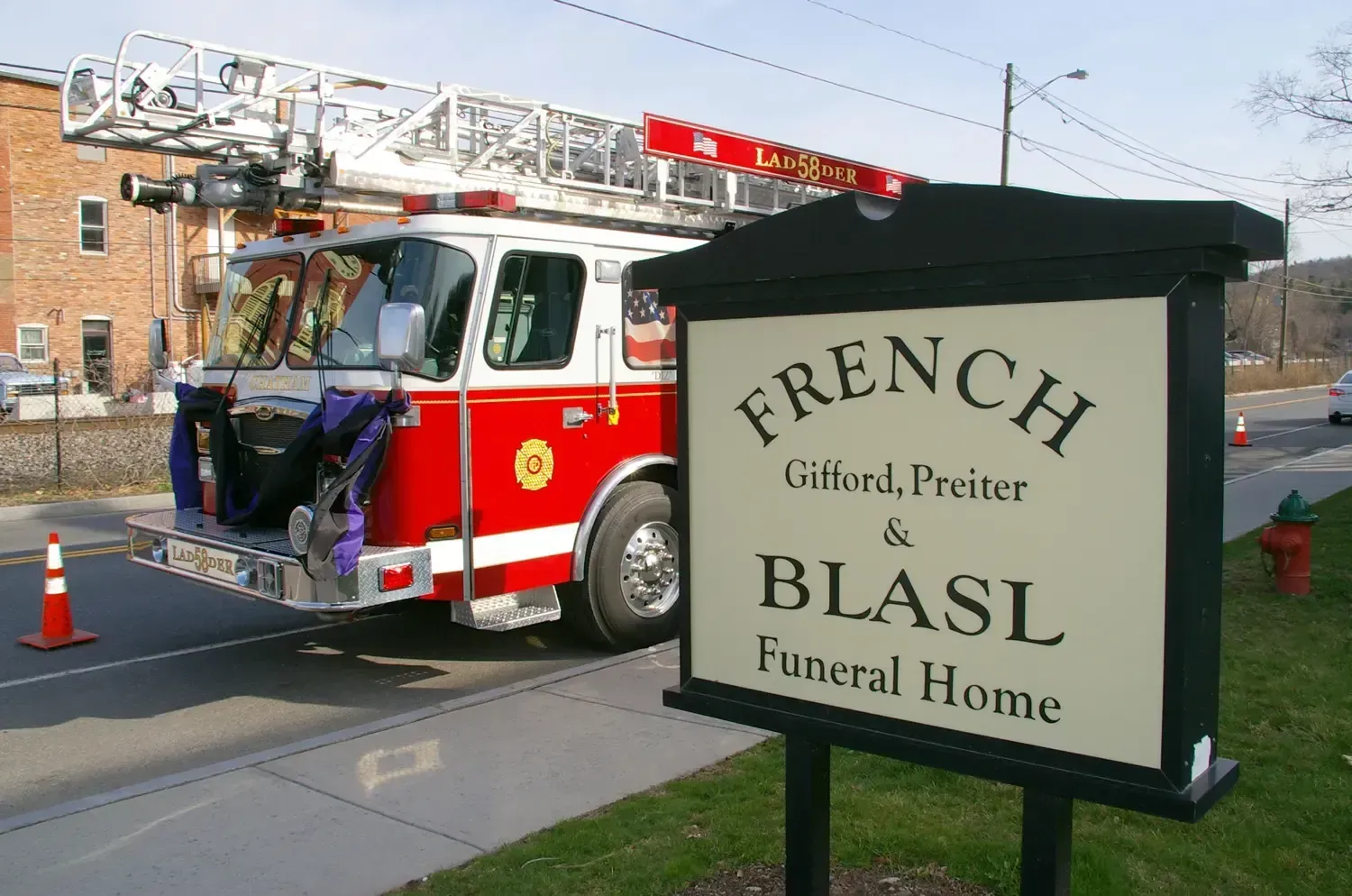 Fire truck outside French Funeral Home sign. Red and white truck, black sign, brick building.