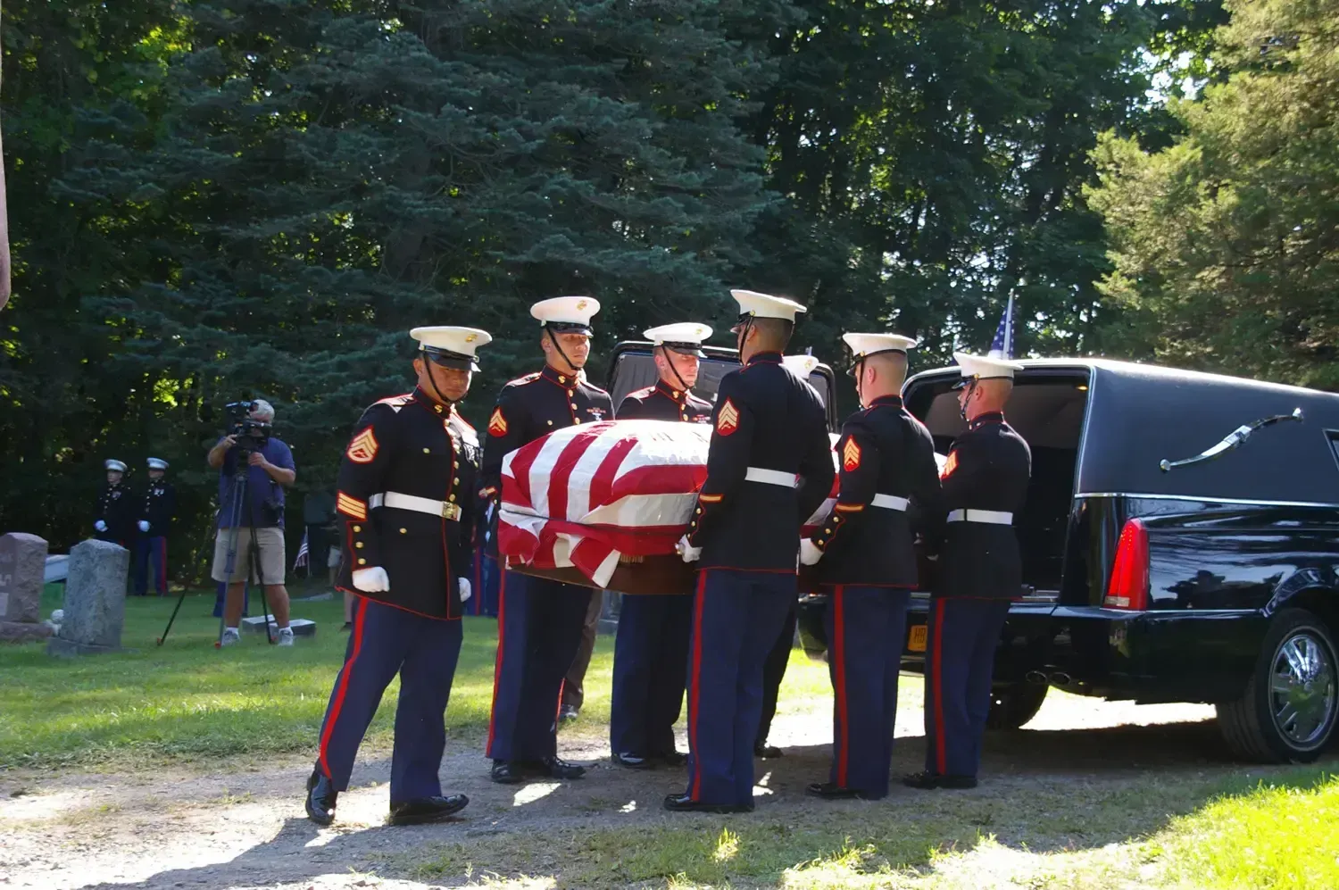 Marines carrying a flag-draped casket from a hearse at a graveside funeral.