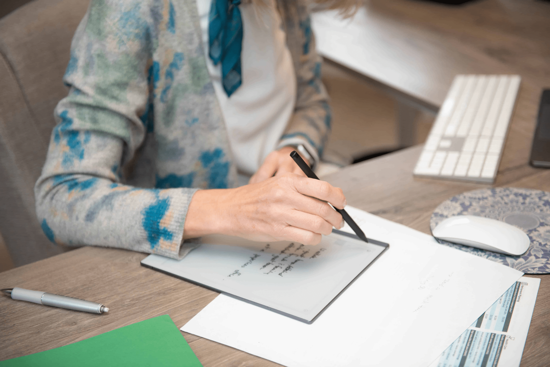 A woman is sitting at a desk writing on a tablet.