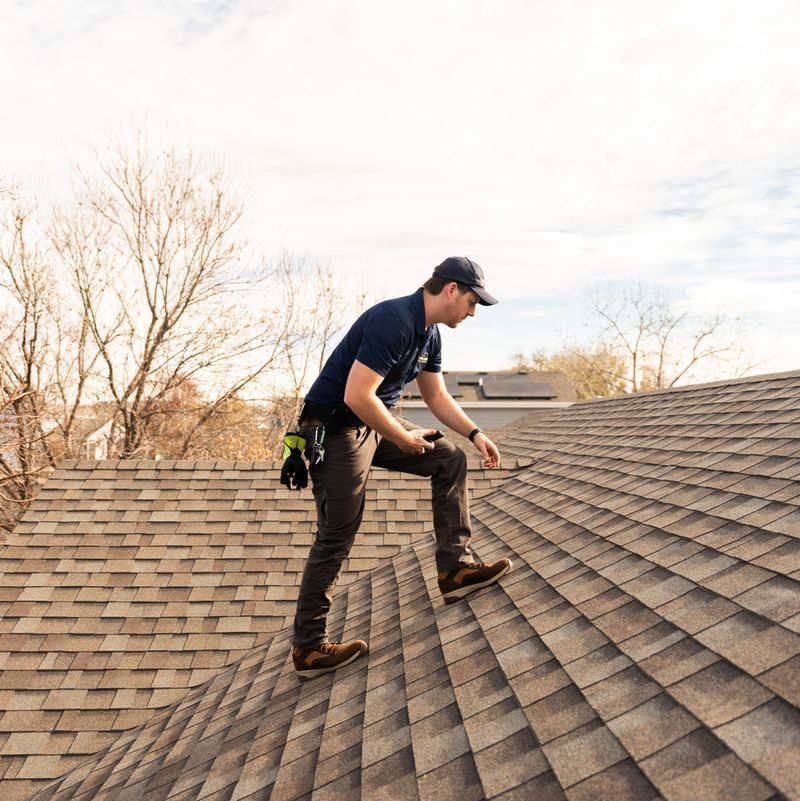 A man is standing on top of a roof inspecting it.