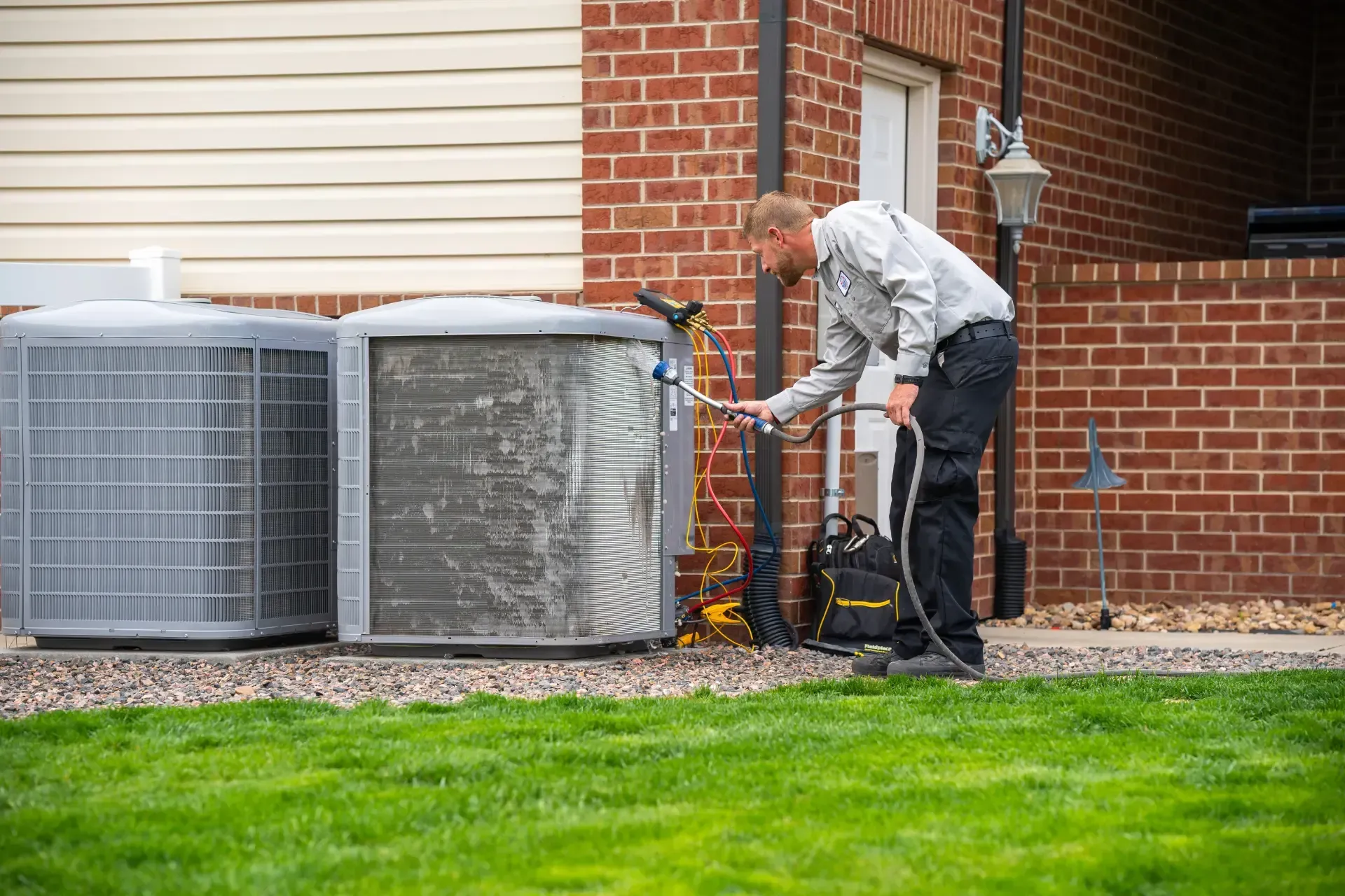 A man is working on an air conditioner outside of a brick house.