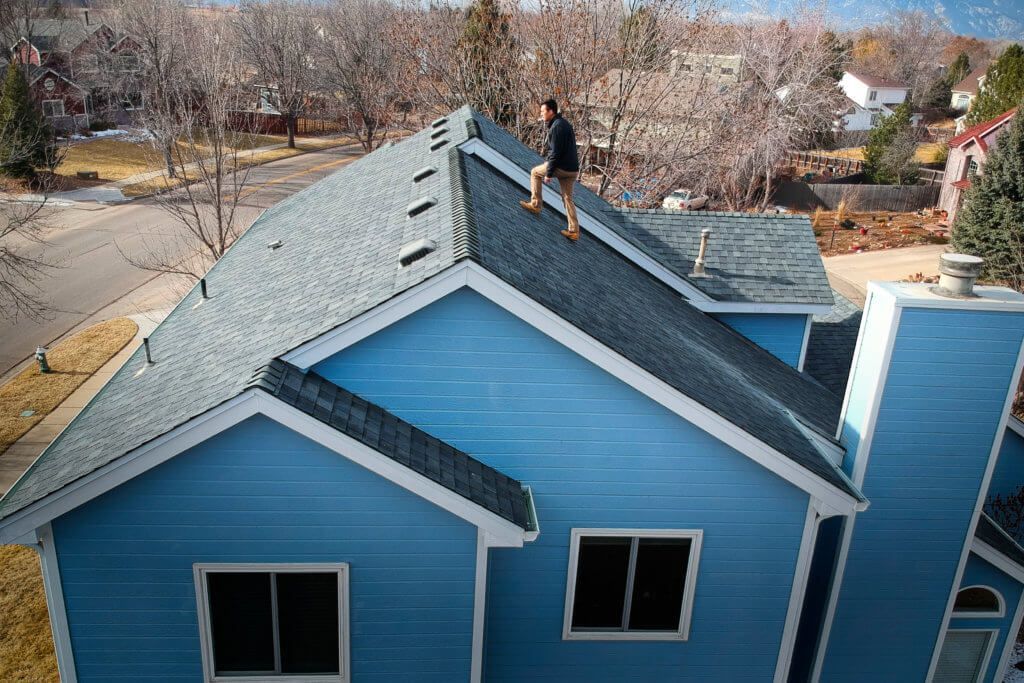 A man is sitting on the roof of a blue house.