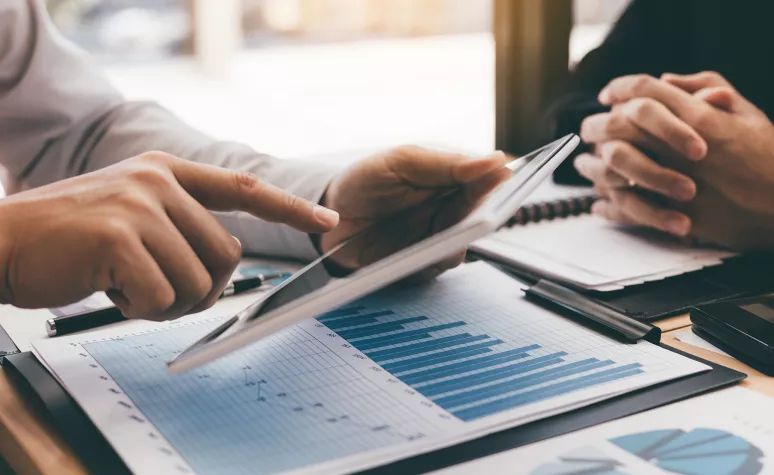 Two people are sitting at a table looking at a tablet.