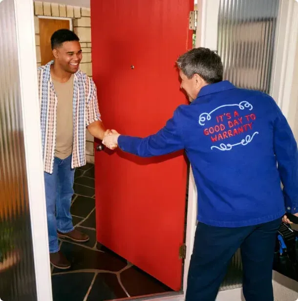 A man wearing a blue jacket that says it 's a good day to warranty shakes hands with another man