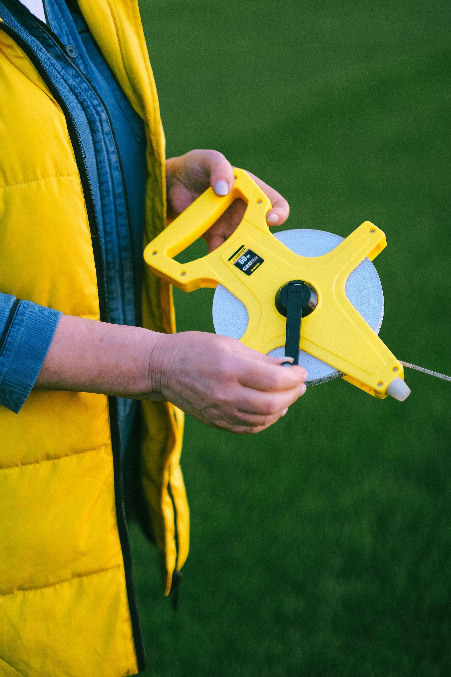 A person in a yellow vest is holding a yellow tape measure.