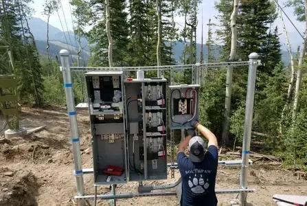 A man is working on an electrical box in the woods.
