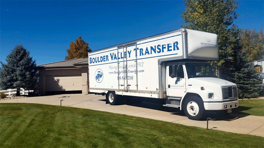 A white moving truck from boulder valley transfer is parked in front of a house.