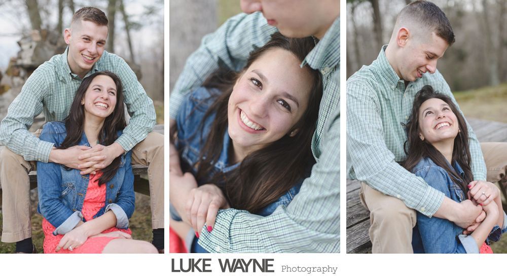 Couple embracing outdoors; woman smiles up at man, both in casual wear, near trees.