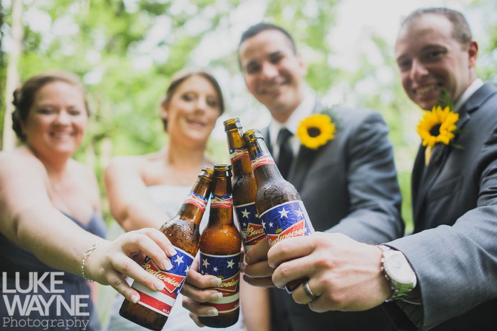 Wedding party toasting with beer bottles in an outdoor setting; sunflowers and smiles.