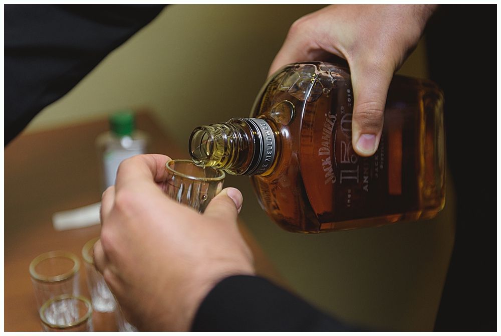 Bride in a white wedding dress smiles, holding a bouquet. A veil flows in the wind under a weeping willow.