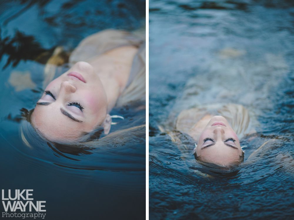 Couple embracing outdoors; woman smiles up at man, both in casual wear, near trees.