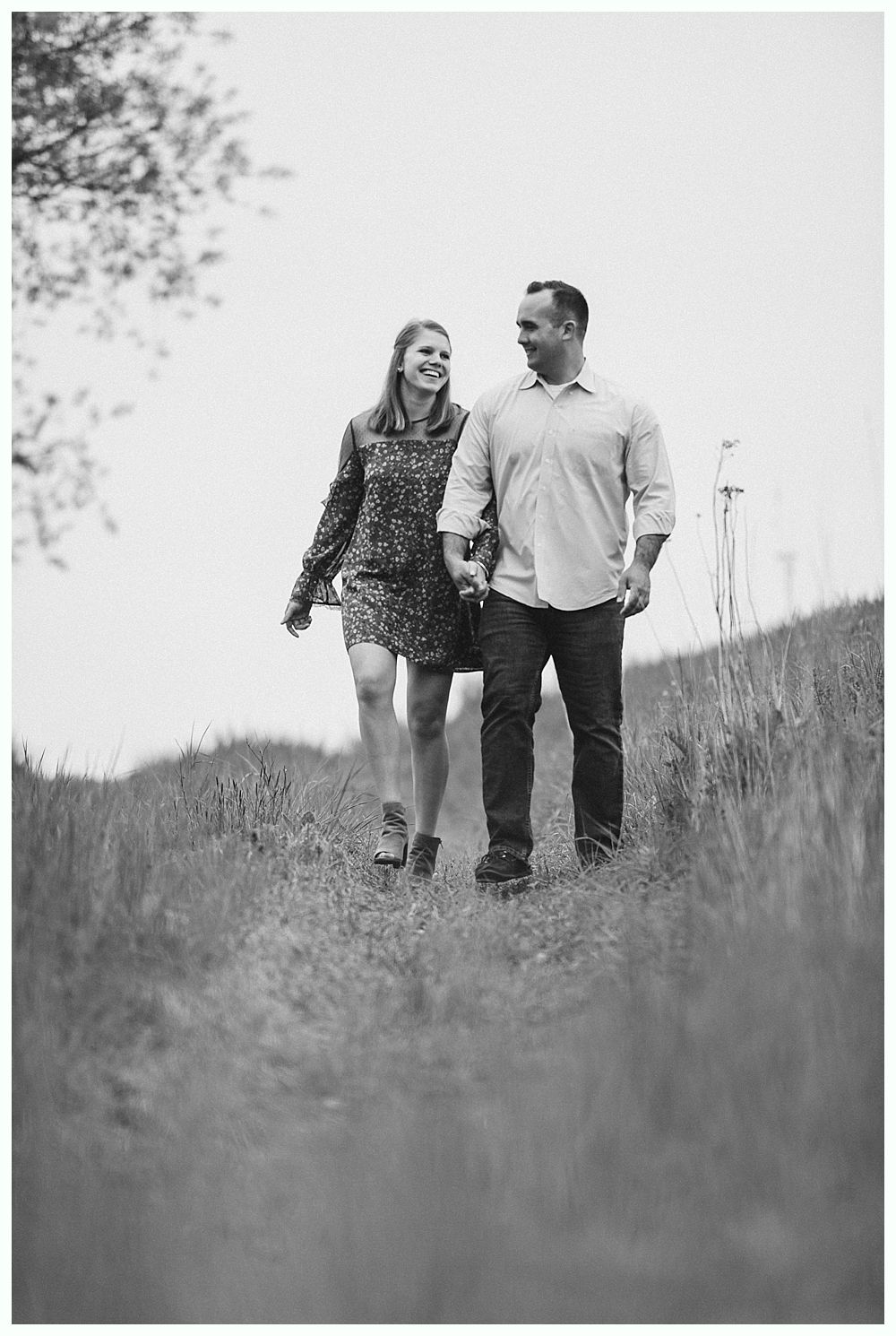 Bride in a white wedding dress smiles, holding a bouquet. A veil flows in the wind under a weeping willow.
