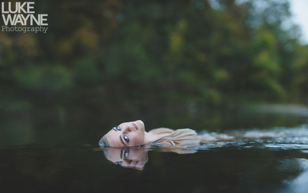 Couple embraces on a rocky outcrop, facing each other. Black and white photograph, cloudy sky, tree on the left.