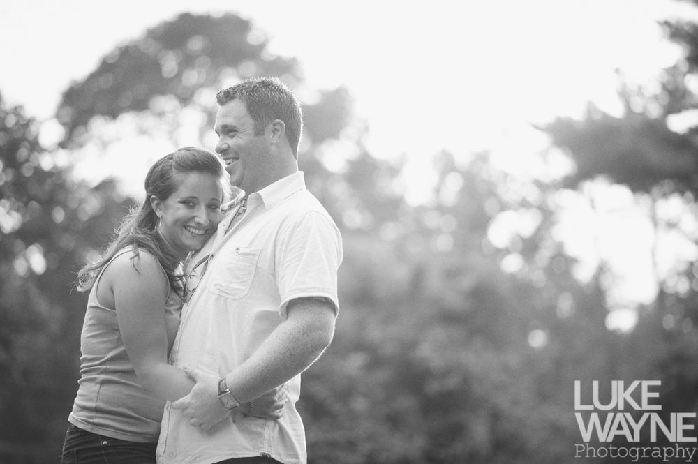 Couple embracing and laughing outdoors, sunlit trees in the background, black and white.