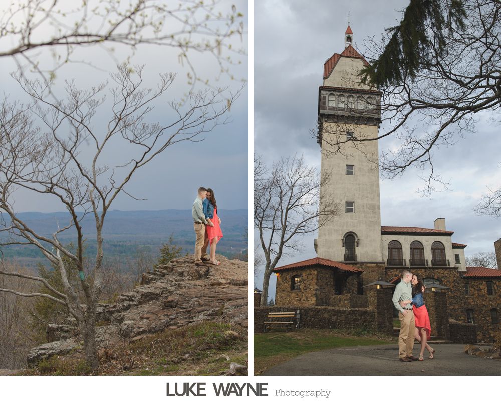 Couple embracing on a rocky peak, with a tower in the background, under a cloudy sky.